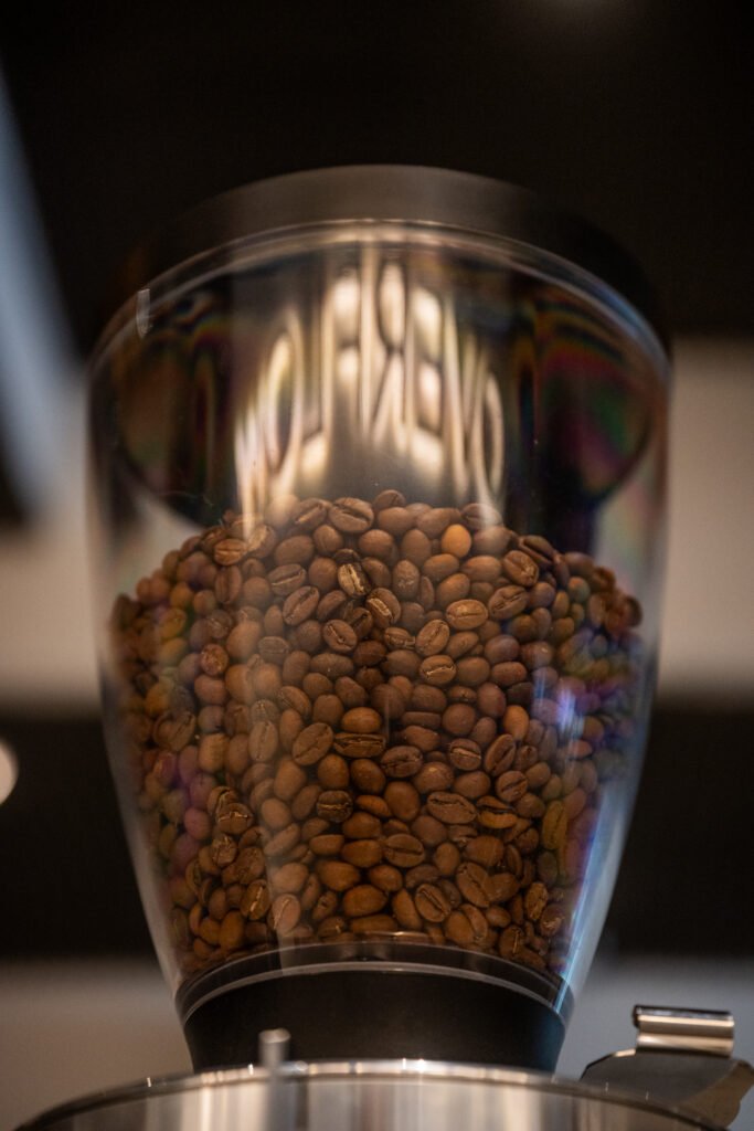 Freshly roasted Arabica coffee beans inside the grinder hopper at Overflow Coffee, a specialty café in Lucknow.