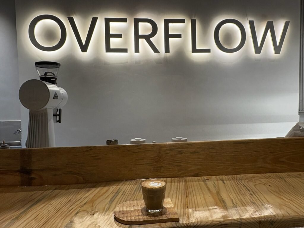 A modern interior view of Overflow Coffee in Lucknow, featuring a professional coffee grinder, minimalist decor, and a freshly brewed latte on a wooden counter.