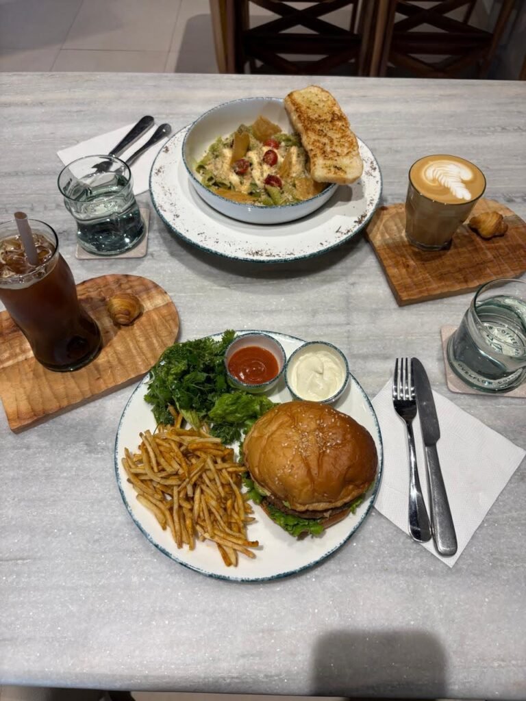 Burger with fries, salad bowl with garlic toast, iced coffee and hot latte on a marble table at Overflow Coffee cafe in Golf City Lucknow