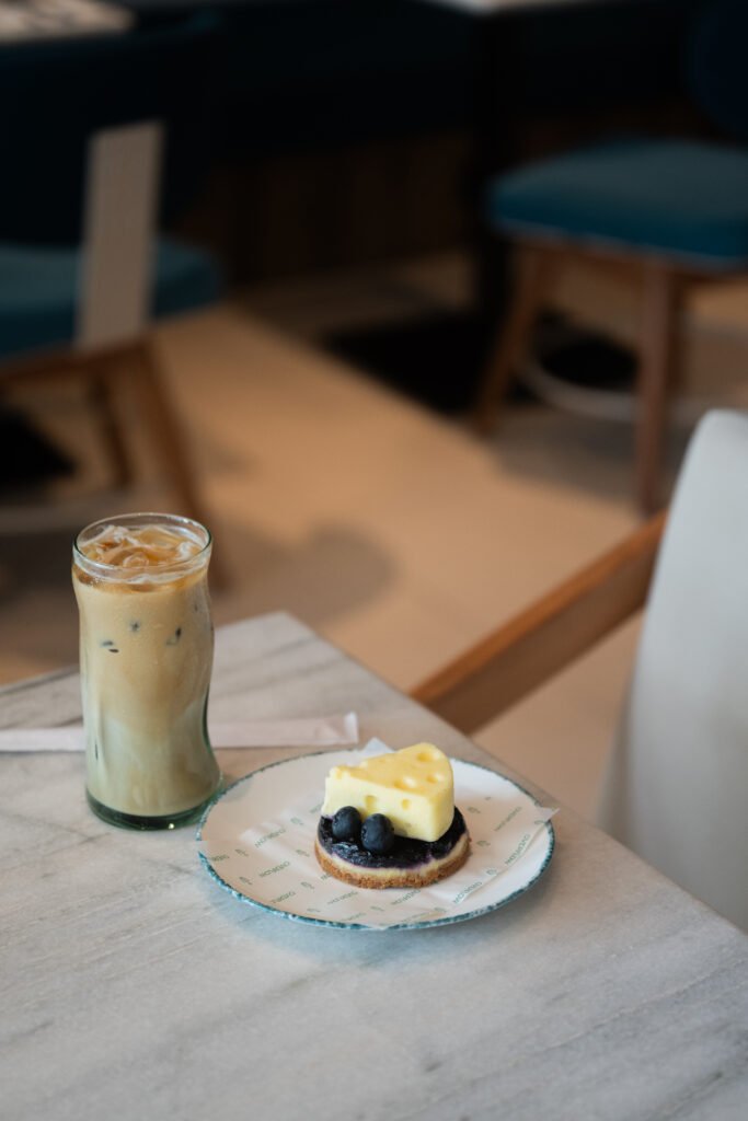 Blueberry cheesecake shaped like a wedge of cheese with an iced coffee at Overflow Coffee, Golf City, Lucknow